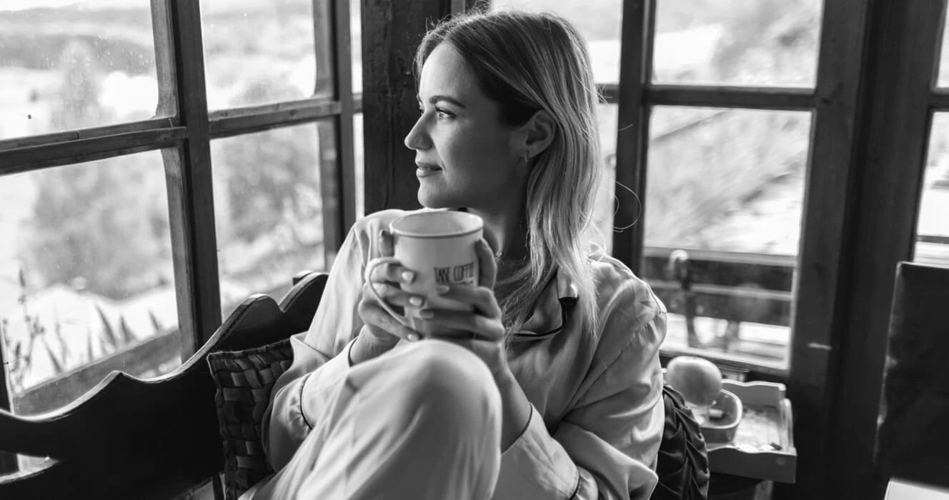 A woman drinking coffee looking out her window